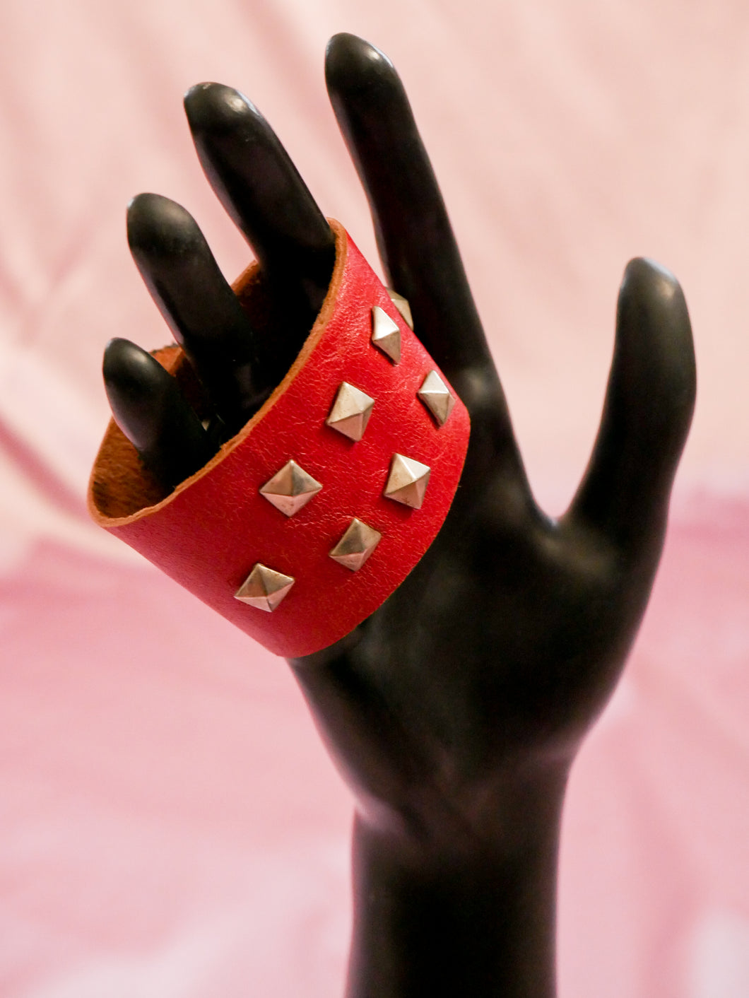 red leather wrap cuff with silver studs on a black mannequin hand women's jewelry